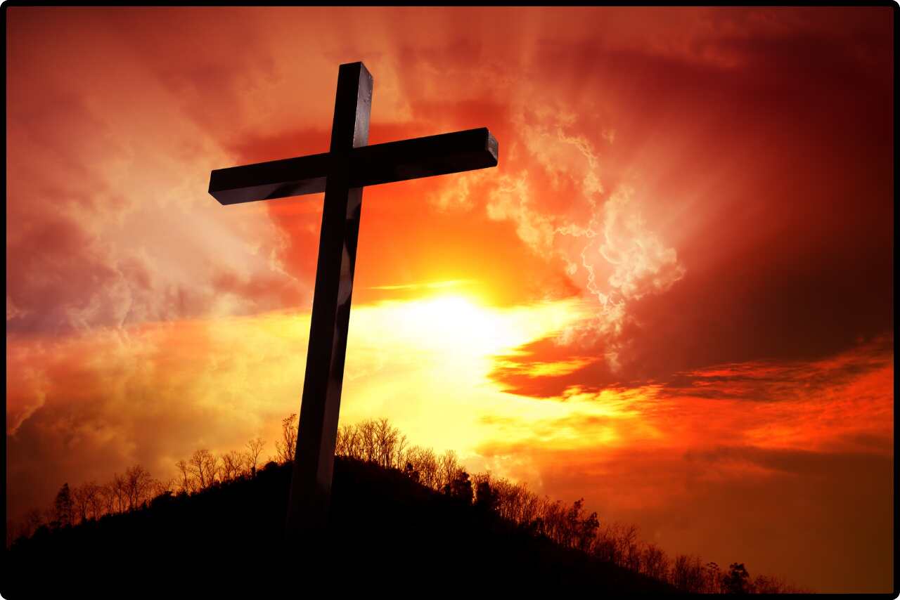 Silhouette of a cross standing tall on a hill against a colorful sunset.